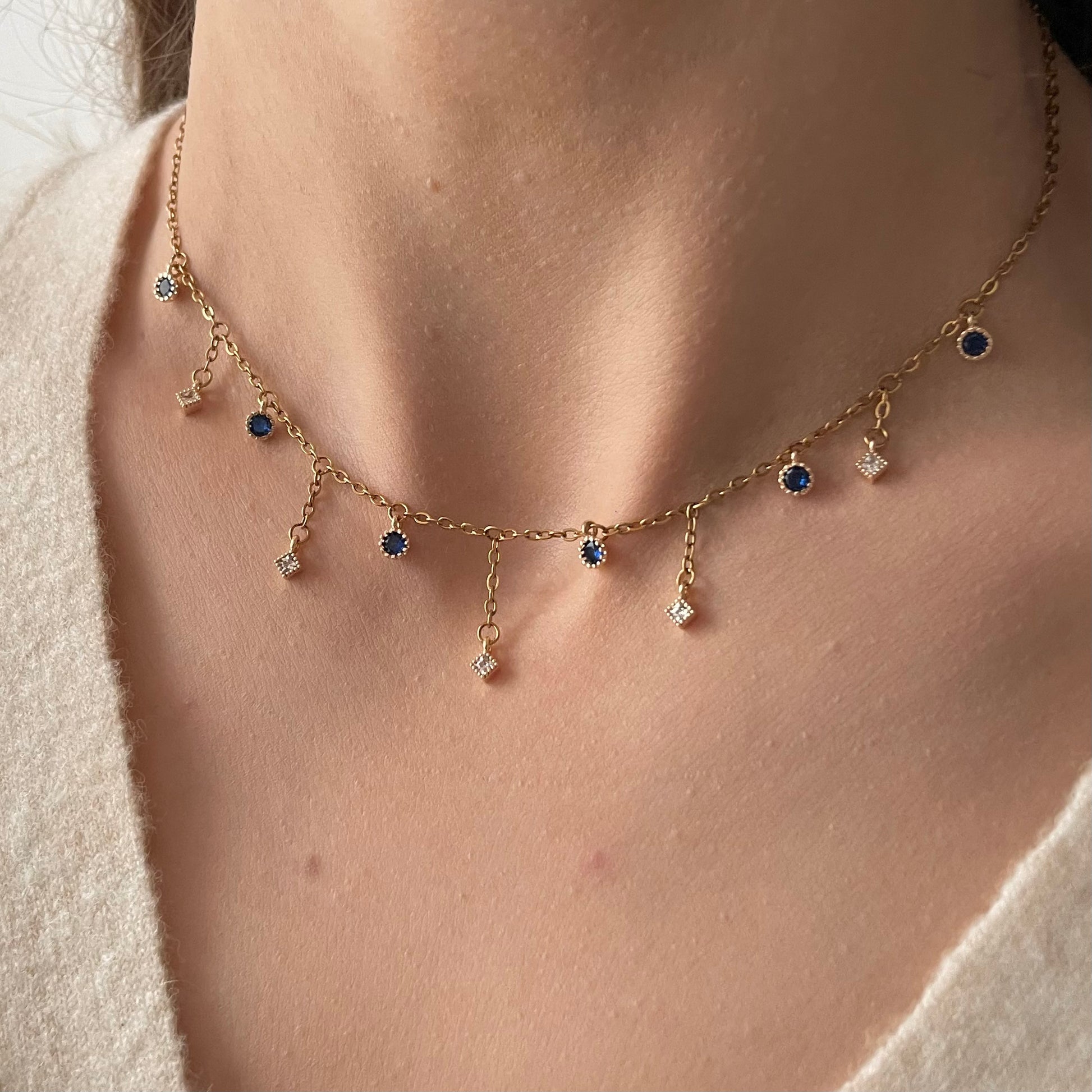 Collier doré en acier inoxydable composé de petits pendentifs ronds bleu foncé et des pendentifs plus longs, en oxyde de zirconium blanc