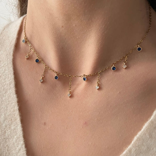Collier doré en acier inoxydable composé de petits pendentifs ronds bleu foncé et des pendentifs plus longs, en oxyde de zirconium blanc